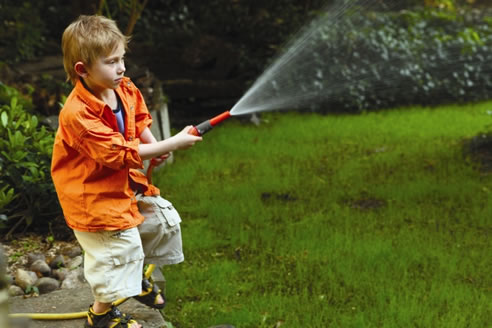 boy watering grass with hose