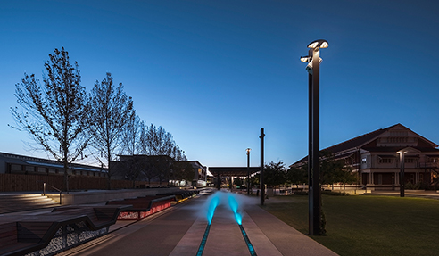 The site includes an Anzac memorial and open space with ceremonial rail line, artworks, shade structures, custom seating, water misting and feature lighting surrounded by the historic workshop buildings and new development sites including a future hotel.